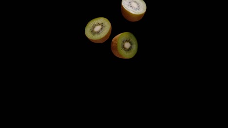 cut in half kiwi fruit falling down isolated on black background, slow motion