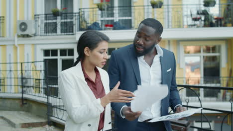 Confident-businessman-and-businesswoman-walking-with-papers-at-urban-street.