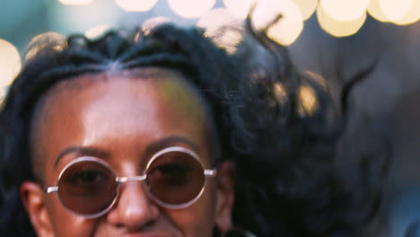 young black woman wearing colourful fringed jacket and sunglasses jumping on the street, close up