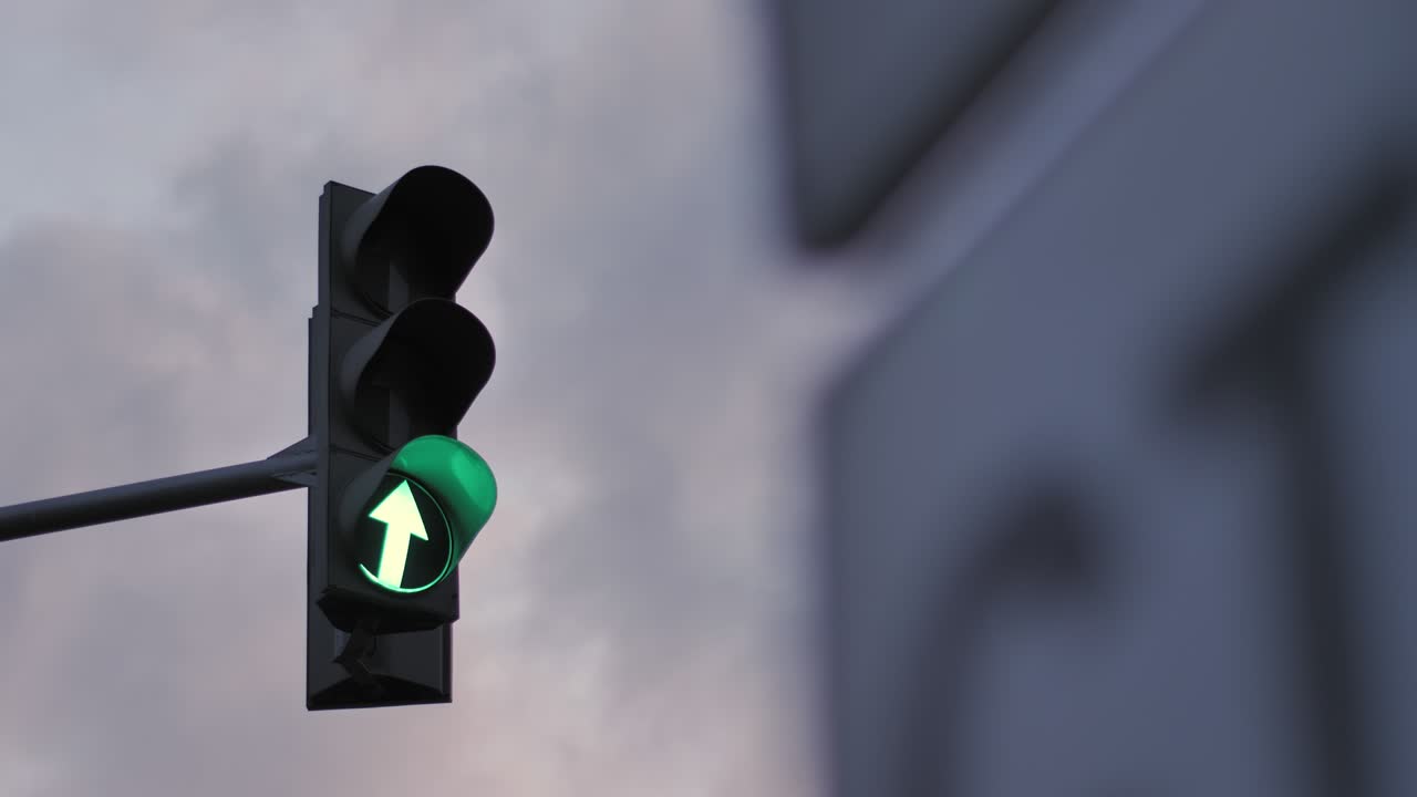 A traffic light against a cloudy sky is lit in green, orange and red. Arrow indicating movement