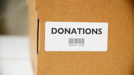 Hands-applying-DONATIONS-Sticker-label-on-a-cardboard-box-with-barcode-donate-here