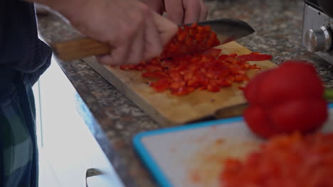 primer plano de manos de hombre con cuchillo cortando pimiento rojo fresco en tablero de madera