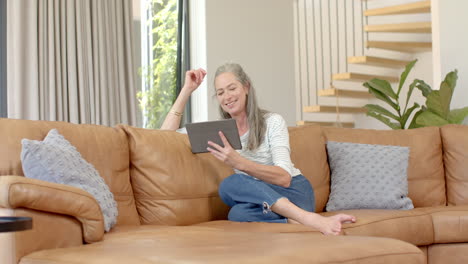 caucasian mature woman sitting on sofa, holding tablet