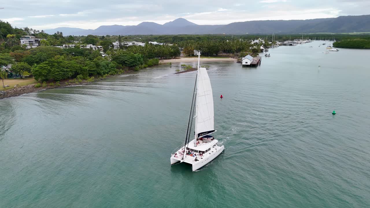 Drone captures a catamaran sailing through calm waters near lush greenery in Port Douglas, Queensland, Australia