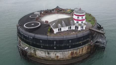 aerial drone flight around the solent fort structure in the english channel in the isle of wight showing the red and white lighthouse and gardens