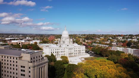 aerial view of the historic rhode island state house with its large dome and white masonry exterior resting on top of the hill surrounded by green and autumn colored trees in downtown.