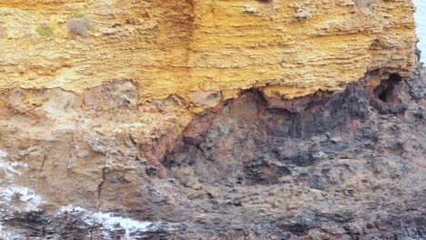 ocean waves hitting a rugged, yellow rock cliff