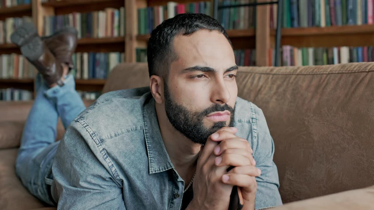 un joven serio de oriente medio está tendido en el sofá y pensando en algo.