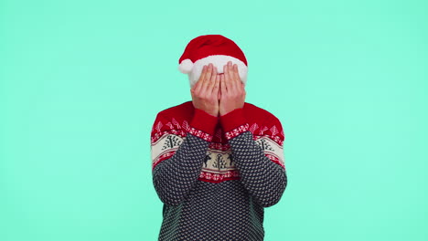 Man-in-sweater-Santa-Christmas-hat-fooling-around-having-closing-eyes-with-hand-and-spying-through