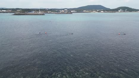 drone aerial view in south korea countryside flying over the sea with green island rocky shallow area haenyeo women divers fishing jeju island cloudy