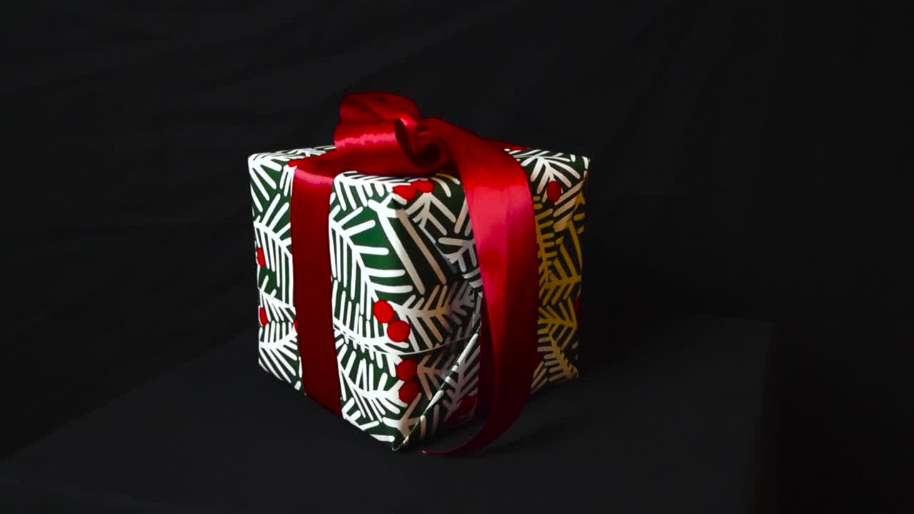 imagens de close-up ou close-up de um presente de natal embrulhado ou presente em um fundo preto enquanto a câmera se move mais revelando a fita vermelha segurando o presente juntos.