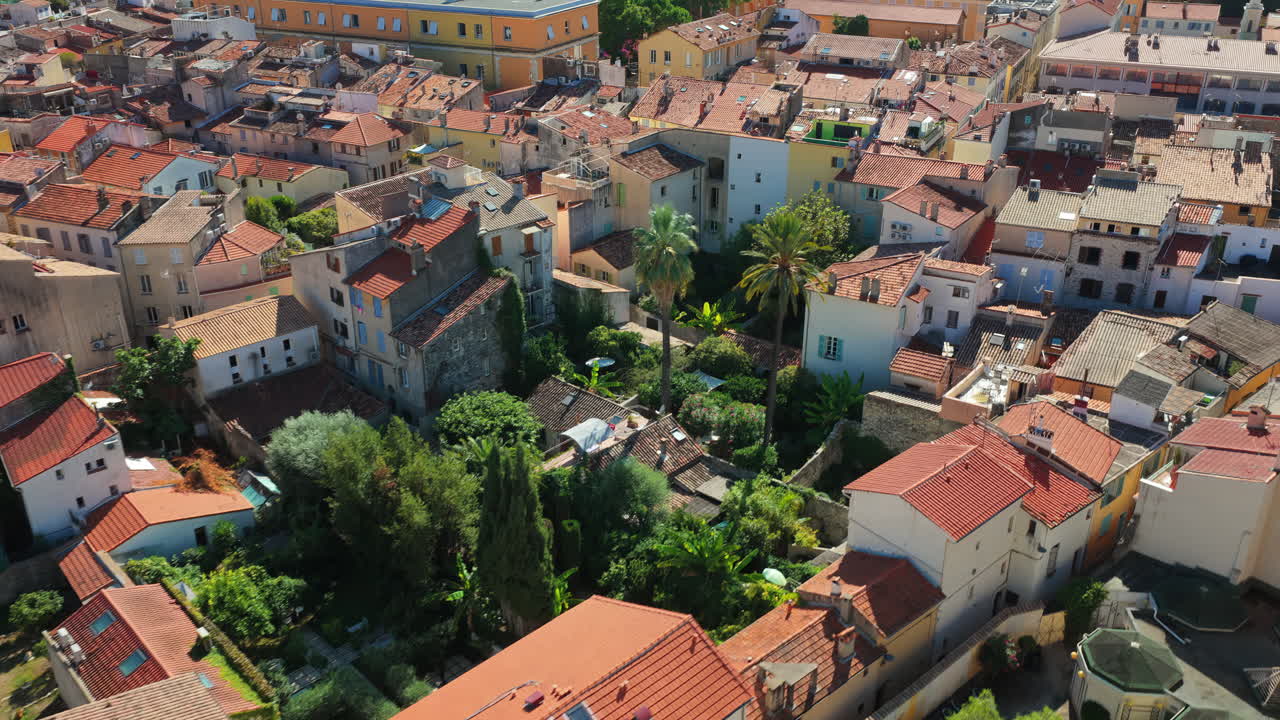 Aerial drone view of Antibes Old Town with palm trees and lush gardens among Mediterranean houses with terracotta rooftops