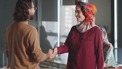 muslim woman greeting male colleague with handshake in office