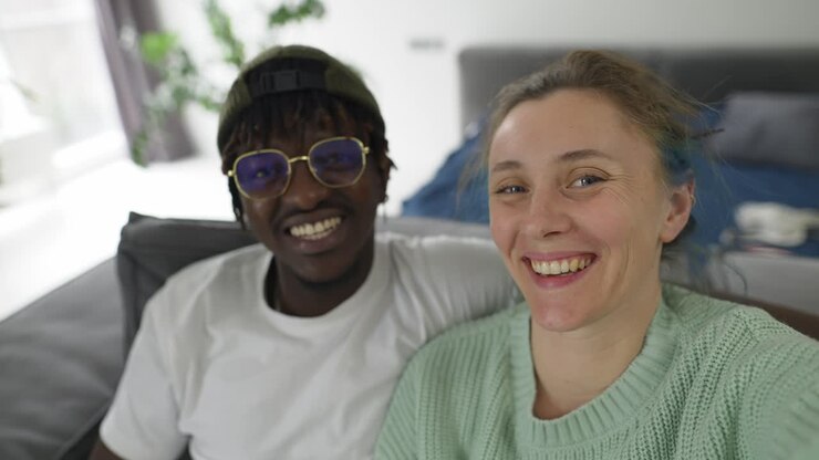 Joyful interracial couple taking selfies with smartphone while sitting together on sofa
