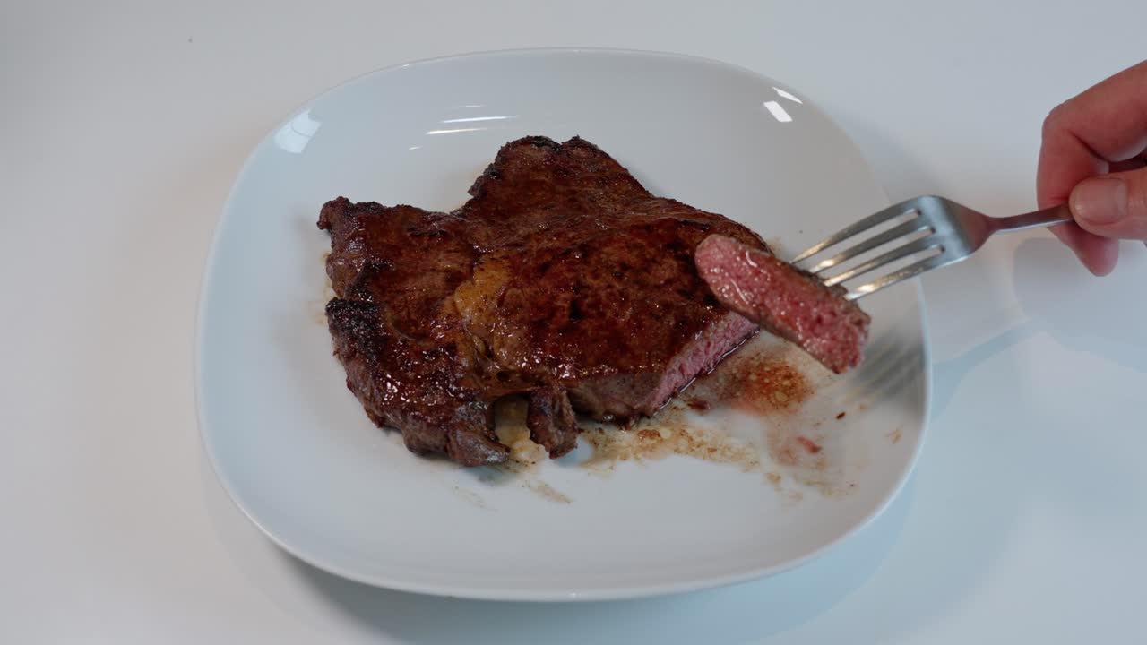 primer plano de un tenedor levantando una jugosa pieza cortada de entrecote cocido medio de un plato blanco, listo para comer