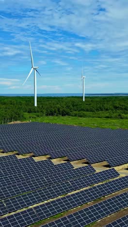 solar panels for renewable energy and windmills in the background, green forest around, cloudy sky, copy space, green energy for a healthy environment, vertical