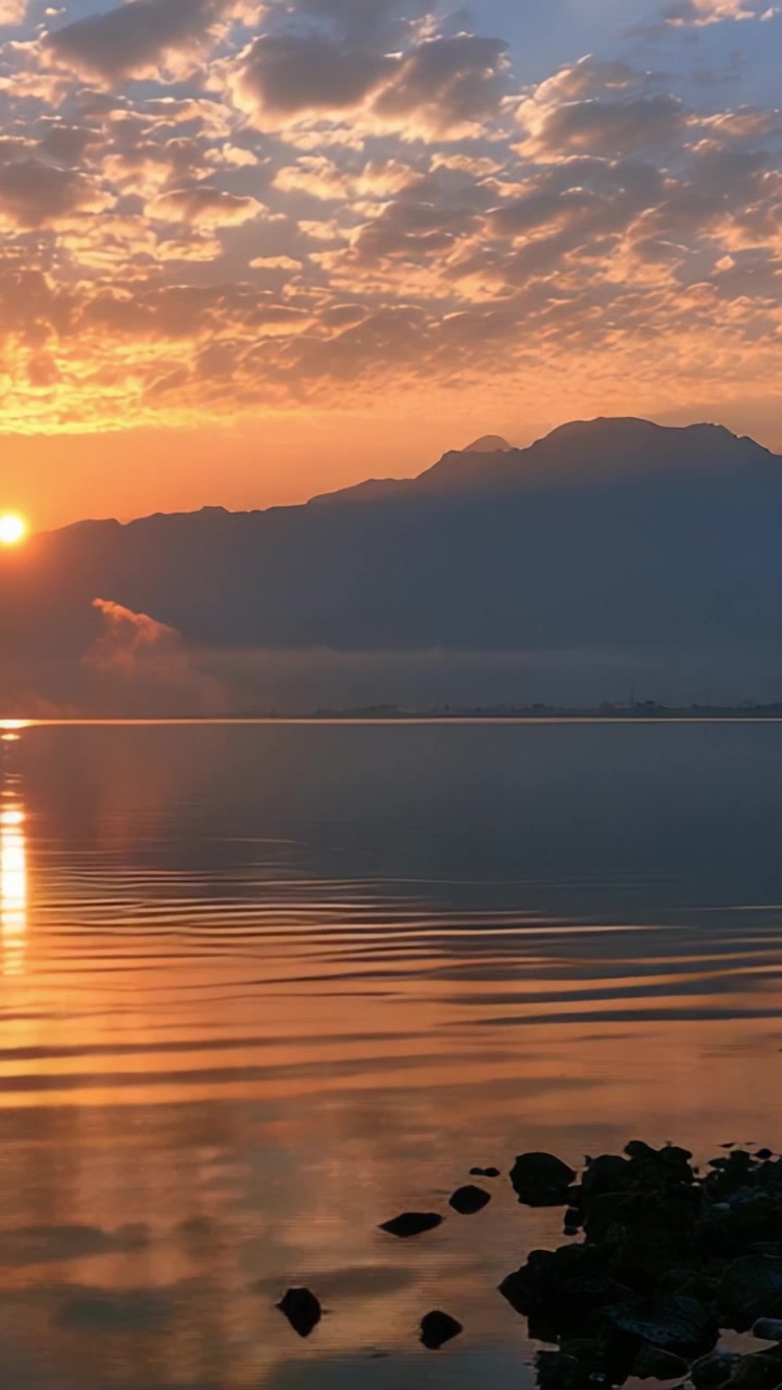 Breathtaking Sunrise at the Tranquil Lake: A Captivating Sky Reflected in Calm Waters with Majestic Mountains in the Background
