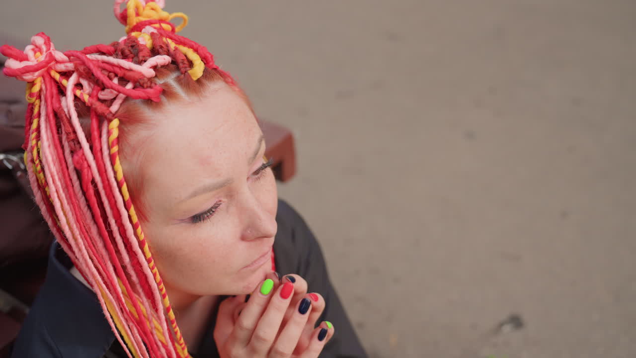 분홍색 드레드록을 한 백인 여성이 손으로 눈물을 닦고, 배낭 옆 나무 벤치에 웅크려 앉아 있어요. 배경에는 포장 도로와 공원 나무가 보이며, 심한 슬픔과 해방을 담은 친밀한 초상화입니다.