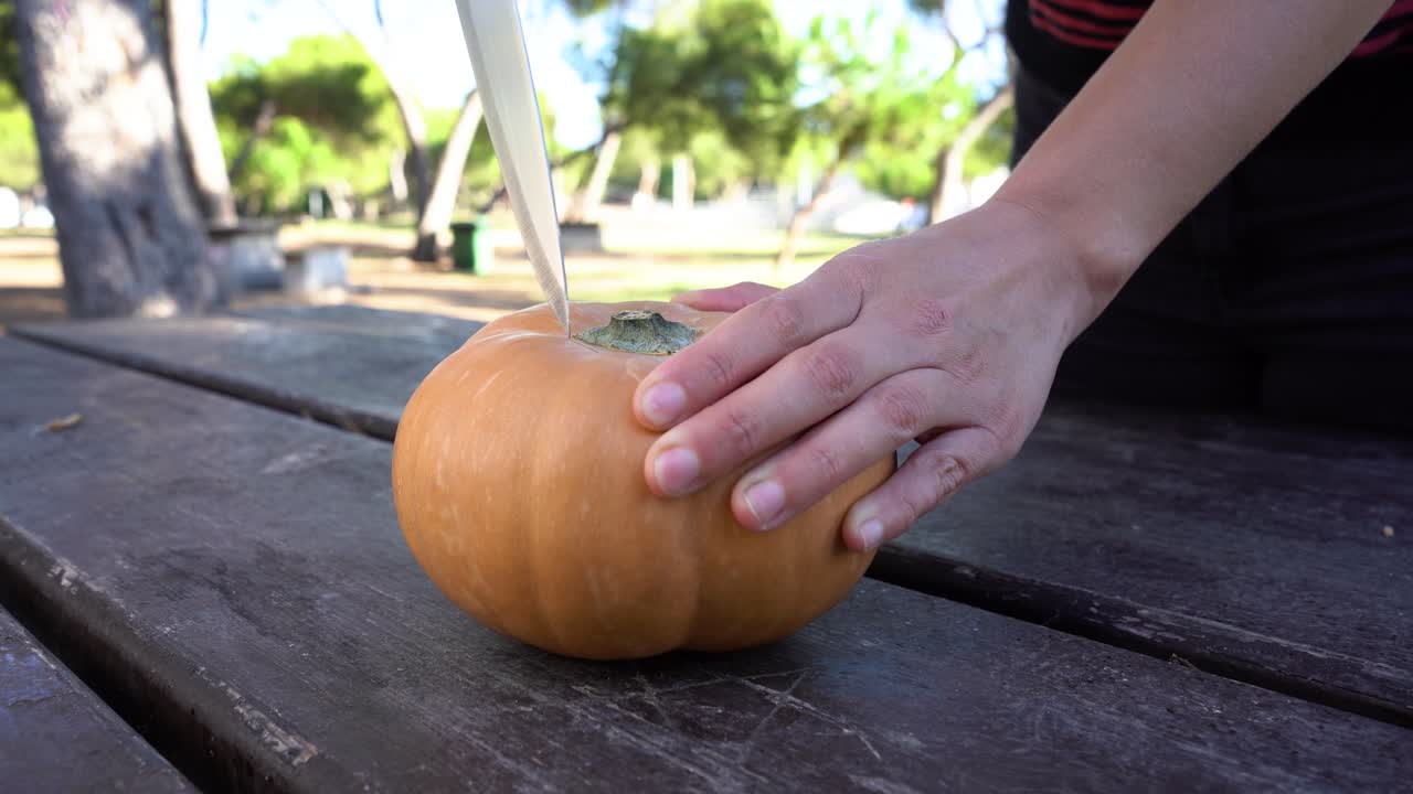 la mujer coloca la calabaza sobre la mesa y comienza a cortar la parte de la tapa