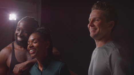 studio portrait of smiling male and female athletes in fitness clothing having fun posing and flexing muscles against in gym with low key lighting