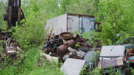 a panning shot of a couple piles of scrap metal rusting away in the forest