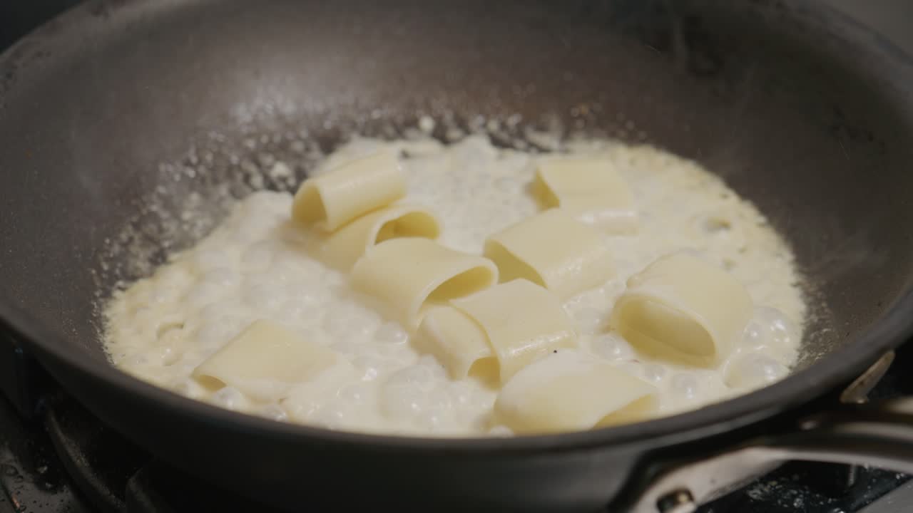 La pasta sobbolle in una salsa bianca in una padella, combinandosi per creare un piatto cremoso