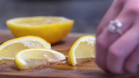 Mujer-Cortando-Jugoso-Limón-Amarillo-En-Cuñas-De-Cerca-En-Una-Tabla-De-Cortar-De-Madera-Con-Un-Cuchillo-Pequeño-Decorado-Con-Flores,-Manos-Con-Esmalte-De-Uñas-Rosa