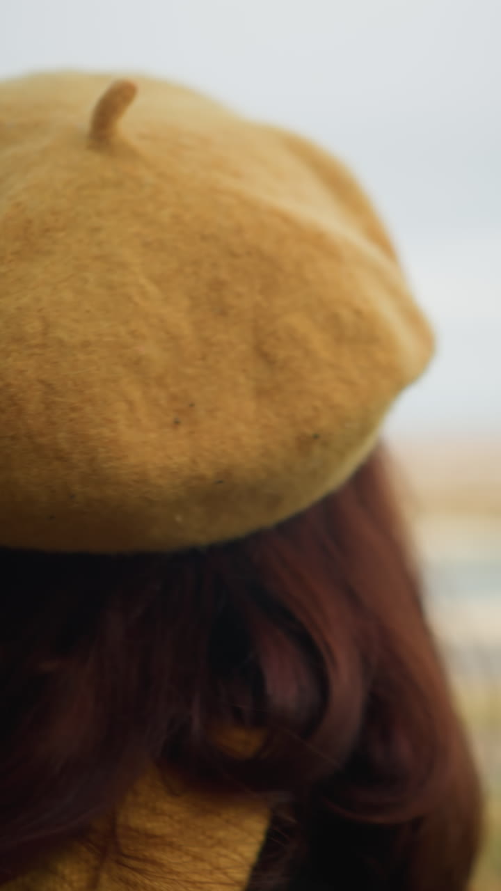 dama con boina amarilla y gafas de sol con abrigo negro, enfocada hacia arriba, con un fondo borroso con un río y árboles de otoño