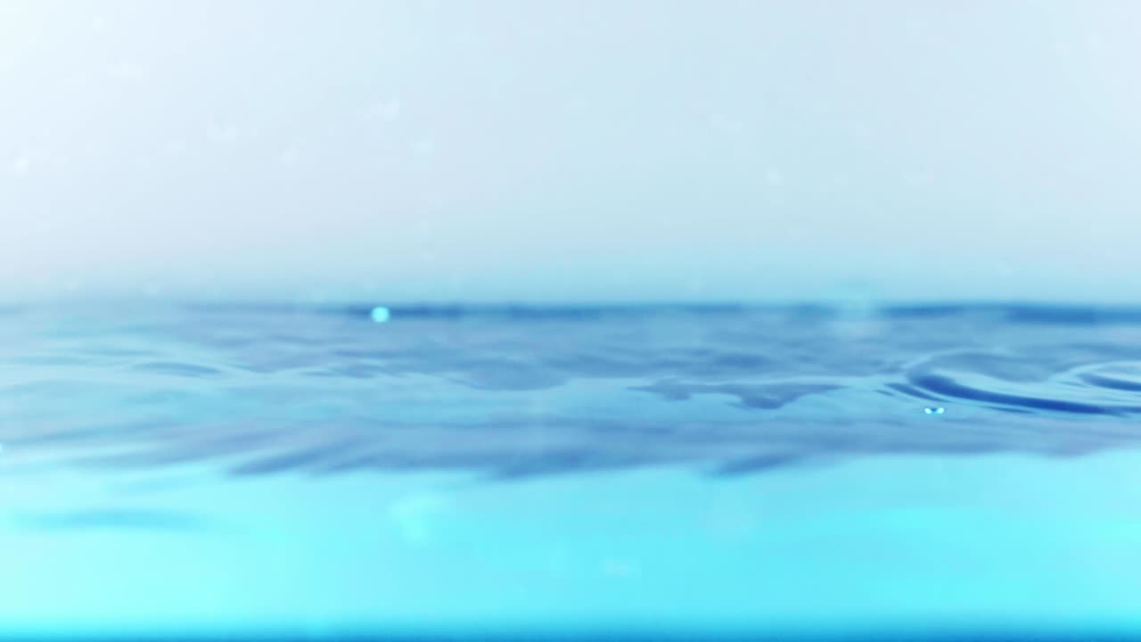 슬로우 모션의 깨끗한 물 표면은 물이 튀는 상점으로 화면을 채우고 기포로 액체 표면을 흔들고 있습니다.