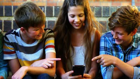 smiling school students sitting on the staircase using mobile phone