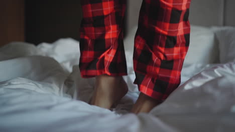 man in pajamas pants jumps on bed in hotel room closeup