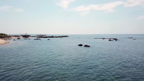 Kleiner-Felsiger-Strand-Mit-Sonnenschirmen-Und-Leuten,-Die-Im-Meer-Schwimmen-Gehen