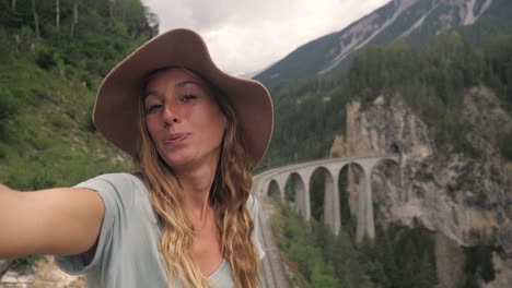 young woman taking selfie with iconic red swiss train and viaduct