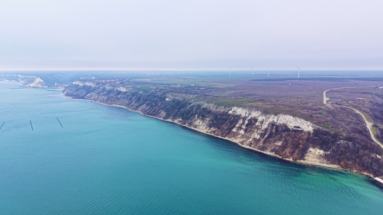 Scogliere a picco lungo la costa con campi verdi sullo sfondo sotto un cielo grigio in una zona costiera