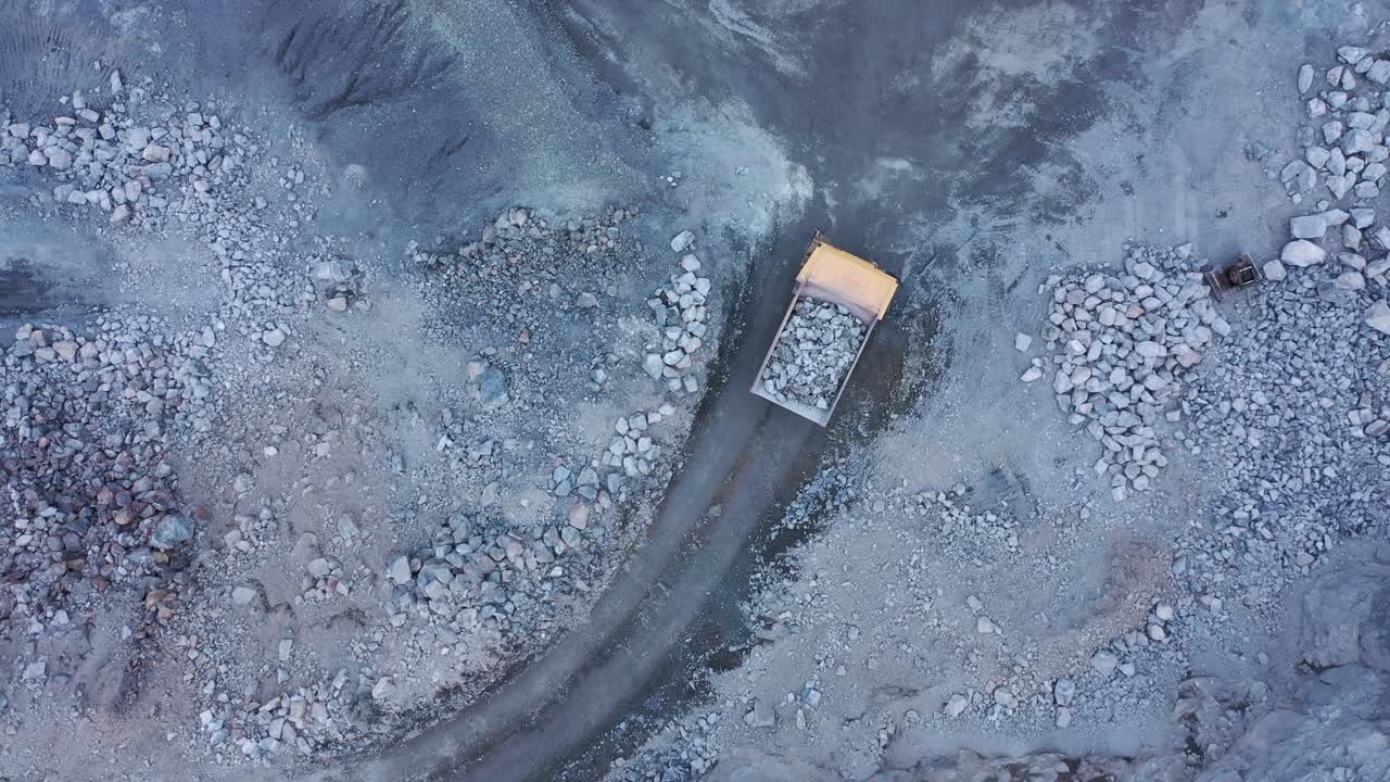 Drone top down shot tracking mining dump truck carrying full load of rocks