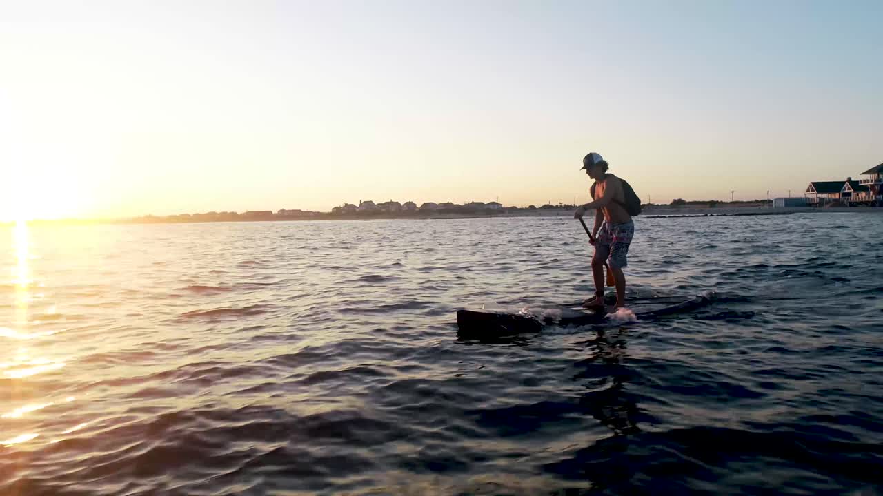 Paddleboarder paddling away into the sunset.