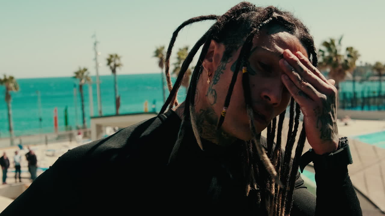 Uomo assorto con dreadlock e tatuaggi sul viso in spiaggia