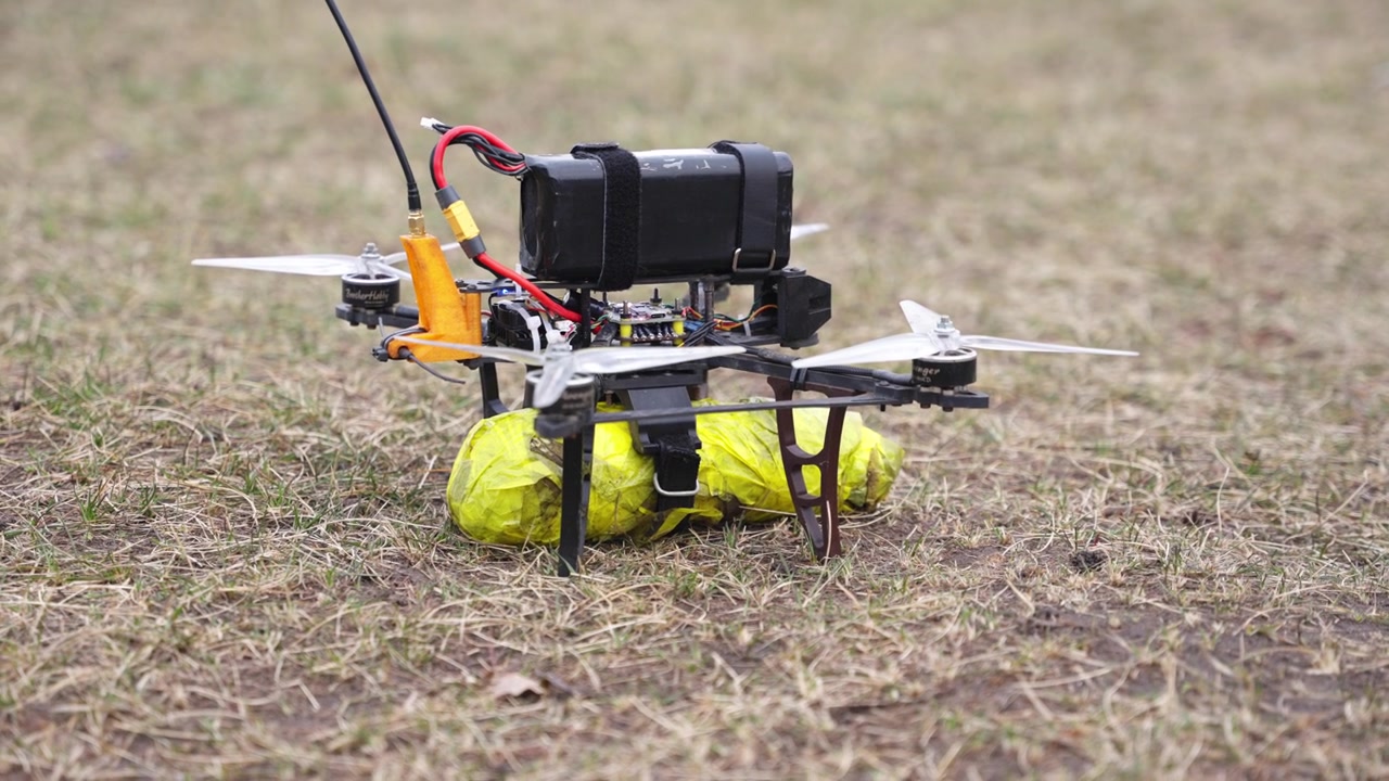 Drone equipaggiato con meccanismo di rilascio che plana stabilmente sopra una superficie di terra in un ambiente di addestramento.