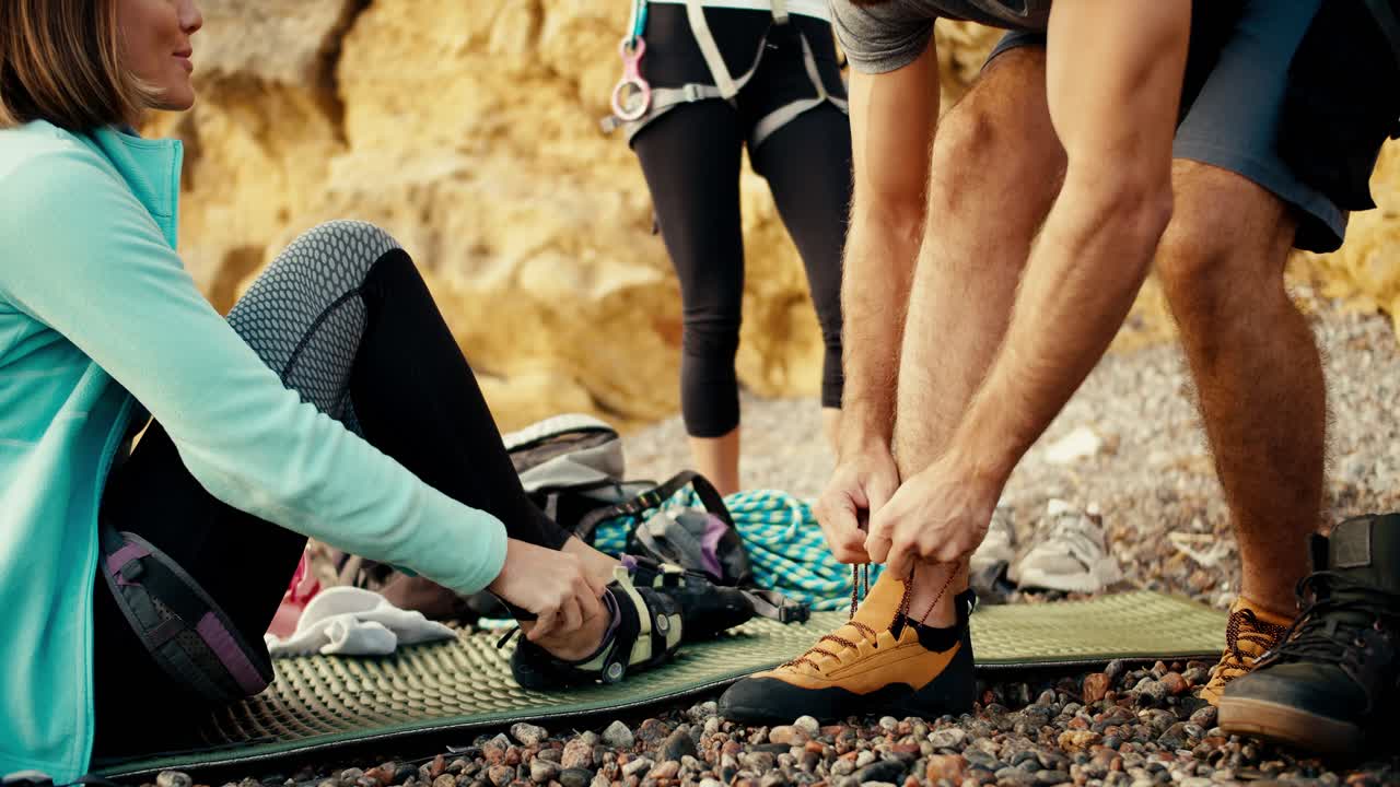 un primer plano de un tipo que se pone zapatos especiales para escalar rocas y atarlos en un grupo de escaladores en una orilla rocosa cerca de las rocas amarillas