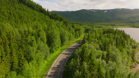 drone follows campervan driving along winding road in mountains past lake, norway