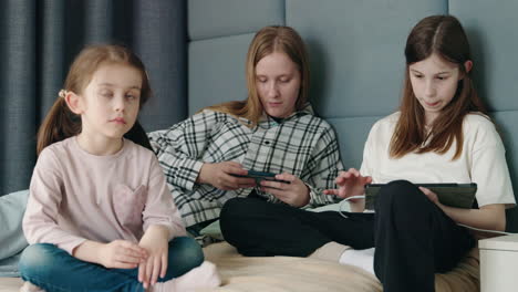 teenage sisters and young sister using digital devices in a bedroom