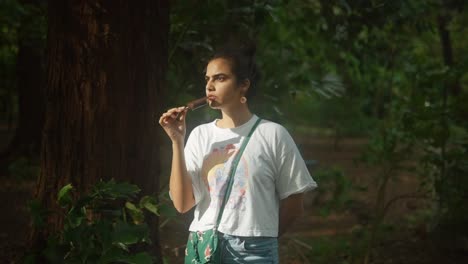 young teenage girl eating chocolate bar ice cream at the park - the concept of vacations, carefree, and relaxation