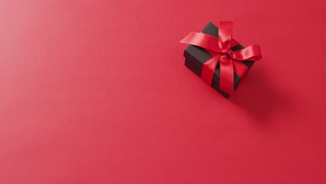 black gift box with red ribbon on red background with copy space