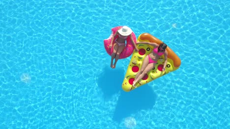 drone: two friends lying on floaties spend a carefree day at a pool party.