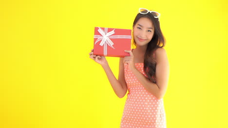 mujer bastante asiática mostrando caja de regalo de cumpleaños, cámara lenta de chica elegante, aislada en fondo amarillo