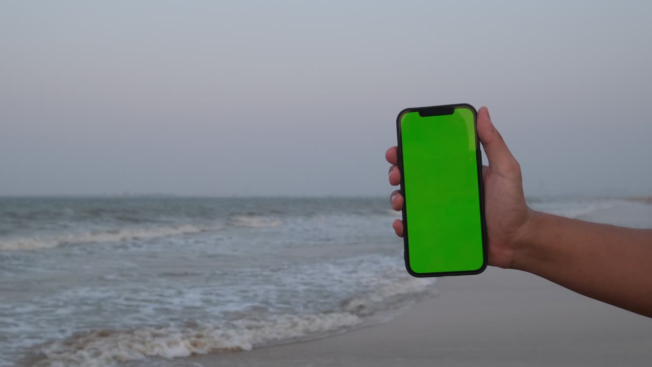hand showing green screen phone on beach