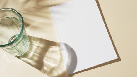 video of glass, shadow of plant over book with blank white pages and copy space on yellow background