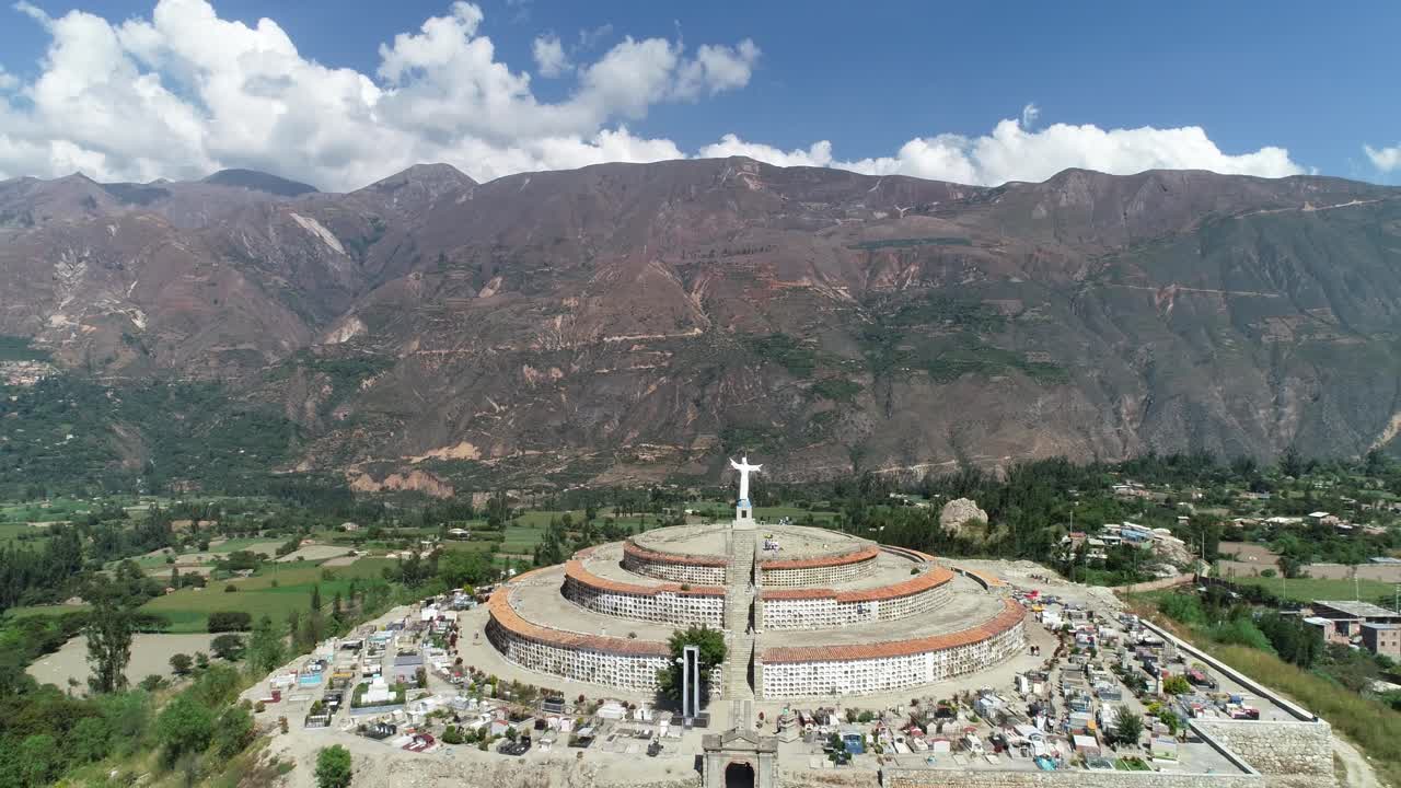 Majestic aerial shot of a circular cemetery crowned by a Christ statue, set against the Andean mountains. Ideal for travel blogs, cultural studies, and stock videography