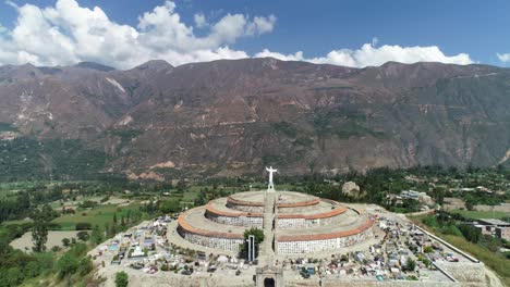 majestic aerial shot of a circular cemetery crowned by a christ statue, set against the andean mountains. ideal for travel blogs, cultural studies, and stock videography