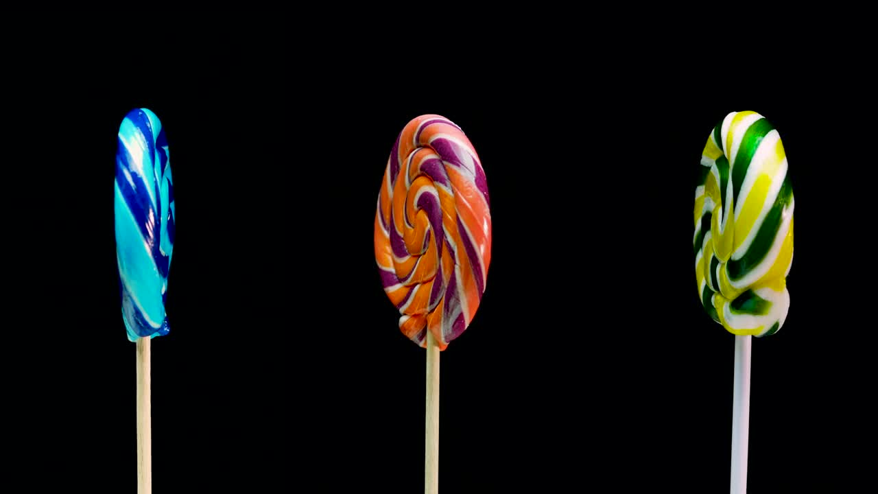 tres piruletas diferentes piruleta verde en un palo girando sobre un fondo negro. espiral de frutas de caramelo de caña espacio de copia